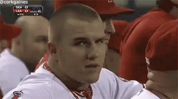 A Man In A Baseball Uniform Is Sitting In A Dugout Looking At The Camera . GIF