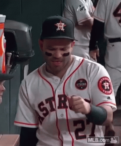 A Man In A Baseball Uniform Is Sitting In A Dugout . GIF