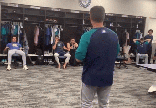 A Man In A Baseball Uniform Stands In A Locker Room With A Mlb Logo On The Wall GIF