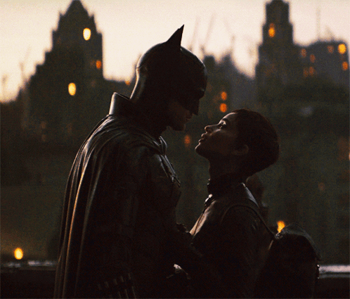 A Man In A Bat Suit And A Woman In A Catsuit Are Looking Into Each Other 'S Eyes GIF