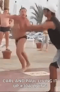 A Man In A Bathing Suit Is Dancing With Another Man In A Hat . GIF