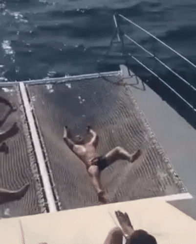 A Man In A Bathing Suit Is Falling Into The Ocean From A Boat . GIF