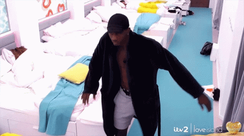 A Man In A Bathrobe Is Dancing In A Room With Lots Of Beds And A Sign That Says Love Island GIF