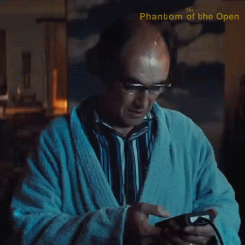 A Man In A Bathrobe Is Playing A Video Game With The Phantom Of The Open Written In The Corner GIF