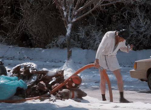 A Man In A Bathrobe Is Pumping Water Out Of A Hose In The Snow GIF