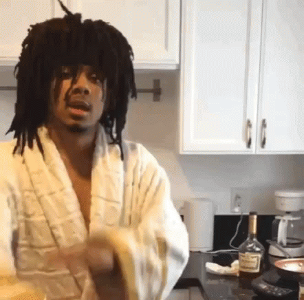 A Man In A Bathrobe Is Standing In A Kitchen With A Bottle Of Hennessy On The Counter GIF
