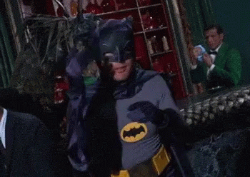 A Man In A Batman Costume Covers His Eyes With His Hands GIF
