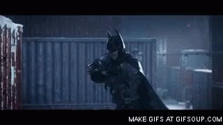 A Man In A Batman Costume Is Holding Another Man In A Dark Room . GIF