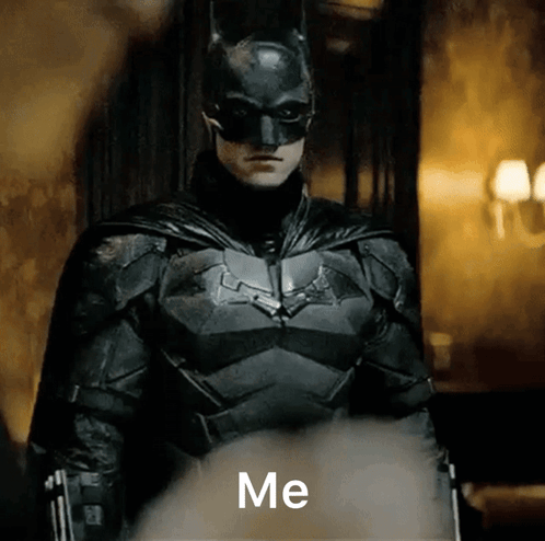 A Man In A Batman Costume Is Standing In A Dark Room And Says Me GIF