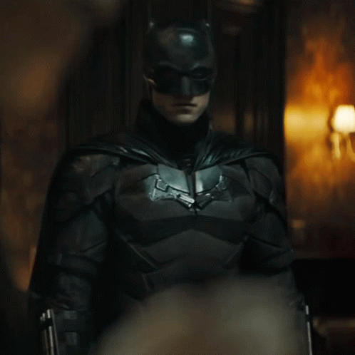 A Man In A Batman Costume Is Standing In A Dark Room GIF