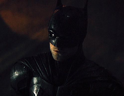 A Man In A Batman Costume Looks At The Camera GIF