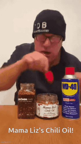A Man In A Beanie Is Eating A Red Pepper Next To A Can Of Wd-40 GIF