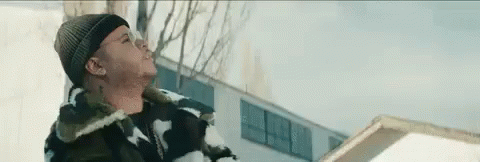 A Man In A Beanie Is Standing In The Snow Near A Building . GIF