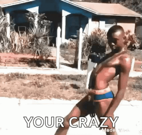 A Man In A Bikini Is Walking Down A Street In Front Of A House . GIF