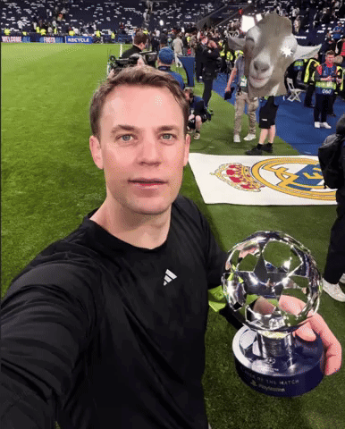a man in a black adidas shirt holds a soccer trophy