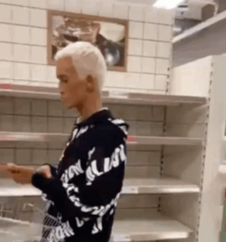 A Man In A Black And White Hoodie Is Standing In Front Of Empty Shelves . GIF