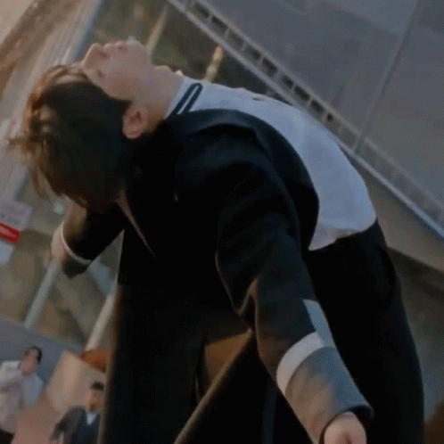 A Man In A Black And White Jacket Is Bending Over In Front Of A Building . GIF