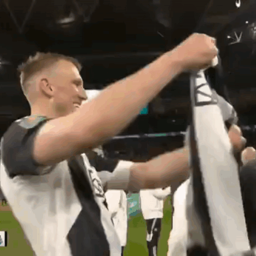 A Man In A Black And White Shirt Holds Up A Scarf With The Letter A On It GIF