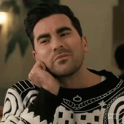 A Man In A Black And White Sweater Is Sitting At A Table With His Hand On His Chin . GIF