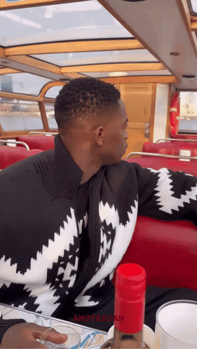A Man In A Black And White Sweater Sits On A Boat With The Word Amsterdam On The Bottom GIF