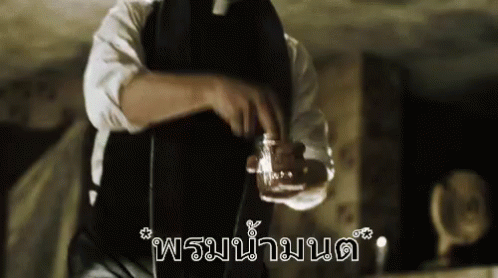 A Man In A Black Apron Is Holding A Glass Of Liquid In His Hand . GIF