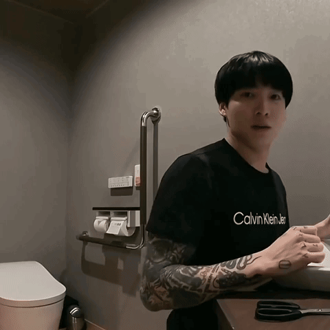 A Man In A Black Calvin Klein T-Shirt Is Standing In A Bathroom GIF