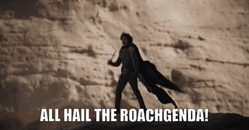 A Man In A Black Cape Stands In The Desert With The Words All Hail The Roachgenda GIF