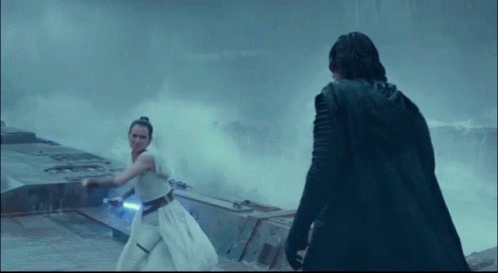 A Man In A Black Cape Stands Next To A Woman Holding A Light Saber GIF