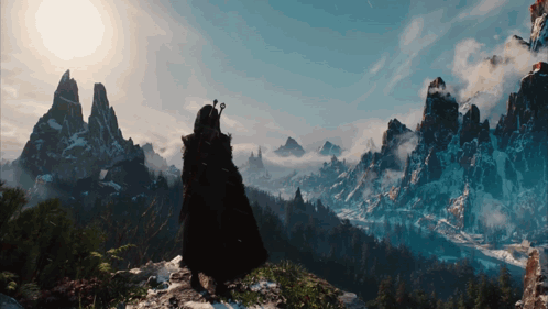 A Man In A Black Cape Stands On Top Of A Mountain GIF