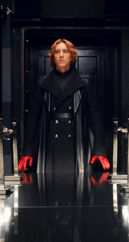 A Man In A Black Coat And Red Gloves Stands In A Doorway GIF