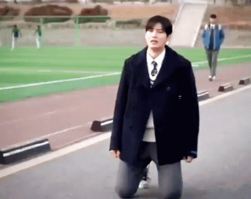A Man In A Black Coat And Tie Is Kneeling On The Ground GIF