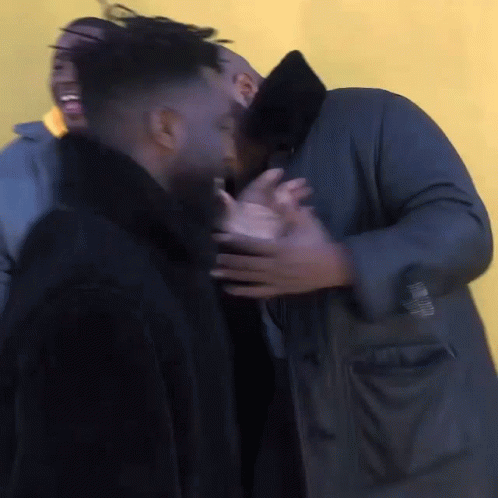 A Man In A Black Coat Is Hugging Another Man GIF