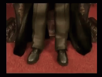 A Man In A Black Coat Is Sitting In A Chair . GIF