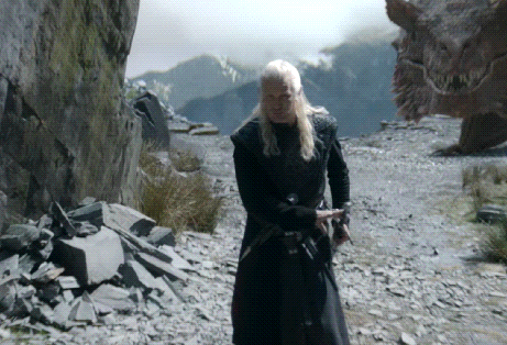 A Man In A Black Coat Is Standing In Front Of A Large Dragon GIF