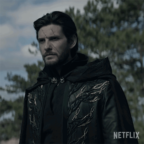 A Man In A Black Coat With Gold Embroidery Is Standing In Front Of Trees And A Sign That Says Netflix GIF