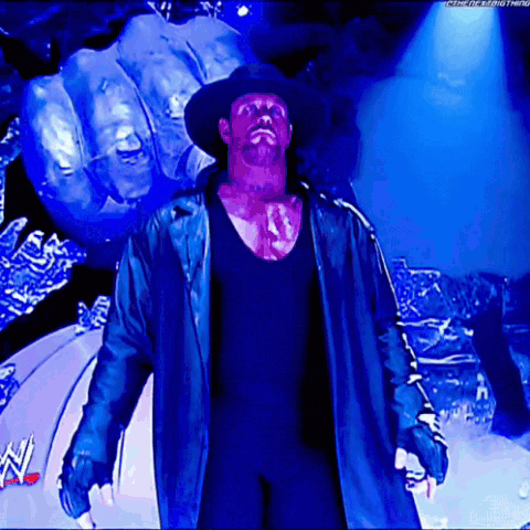 A Man In A Black Hat And A Blue Coat Stands In Front Of A Giant Fist GIF