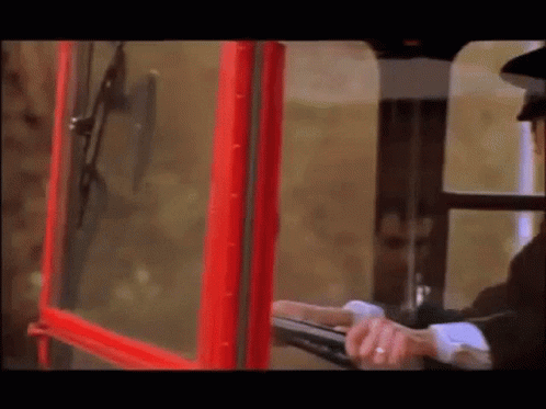 a man in a black hat is looking out of a red telephone booth