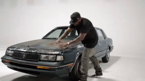 A Man In A Black Hat Is Standing Next To A Car GIF
