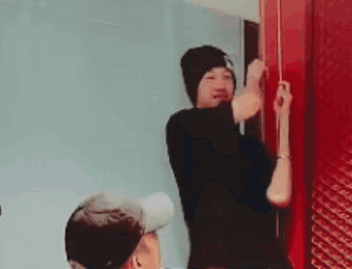 A Man In A Black Hat Is Standing Next To A Red Door . GIF