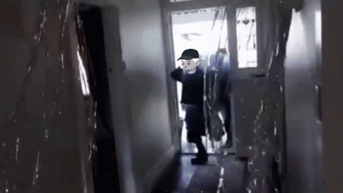 A Man In A Black Hat Is Walking Through A Hallway GIF