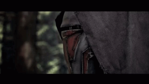 A Man In A Black Hood Is Holding A Red Light Saber In A Dark Forest GIF