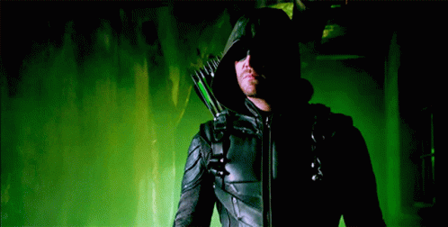 A Man In A Black Hooded Jacket Is Holding A Green Arrow GIF