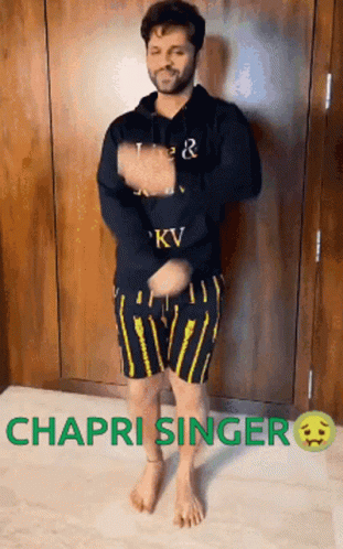 A Man In A Black Hoodie And Yellow Shorts Is Dancing In Front Of A Wall . GIF