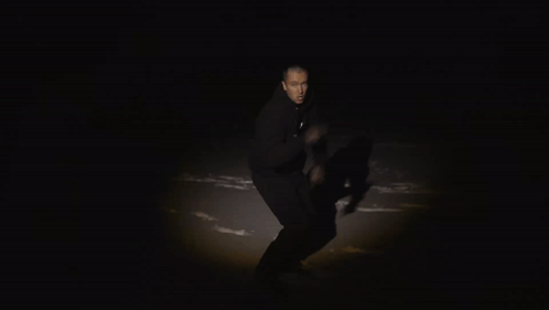 A Man In A Black Hoodie Holds A Piece Of Red Paper With The Number 2123 On It GIF
