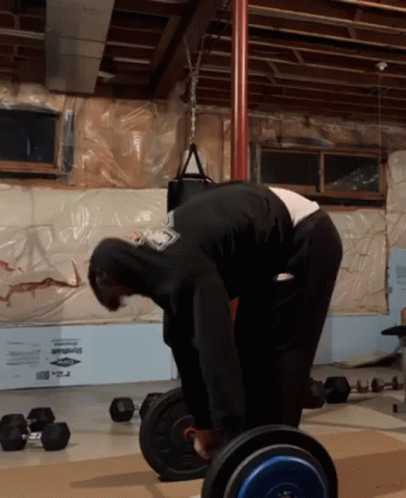 A Man In A Black Hoodie Is Bending Over To Lift A Barbell In A Gym GIF