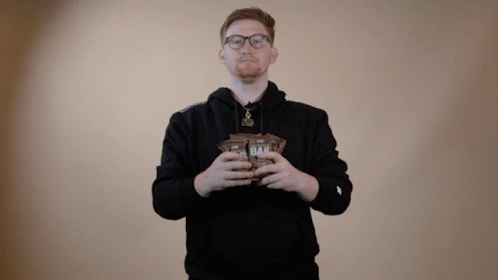 A Man In A Black Hoodie Is Holding A Bag Of Oat Bars GIF