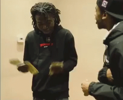 A Man In A Black Hoodie Is Holding A Bunch Of Money While Standing Next To Another Man In A Hat . GIF