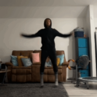 A Man In A Black Hoodie Is Jumping In Front Of A Couch GIF