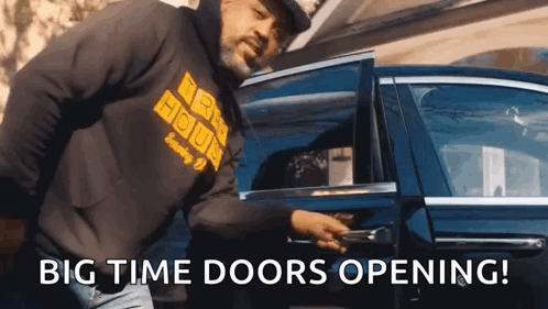 A Man In A Black Hoodie Is Opening The Door Of A Car GIF
