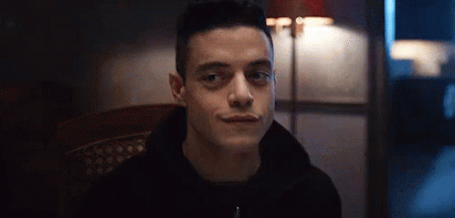 A Man In A Black Hoodie Is Sitting In A Chair And Smiling At The Camera . GIF